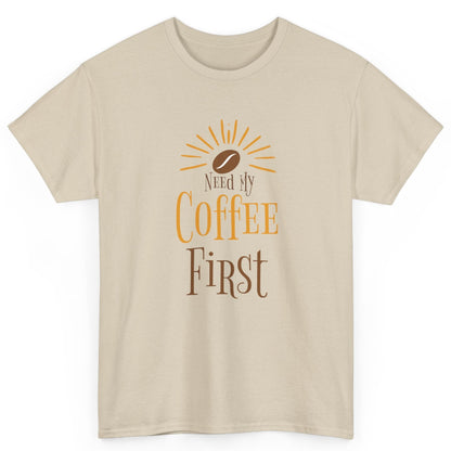 Beige t-shirt with 'Need My Coffee First' text and coffee bean graphic on a white background