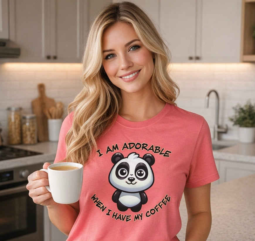Woman in a kitchen wearing a pink t-shirt with a panda graphic and text, holding a coffee cup.